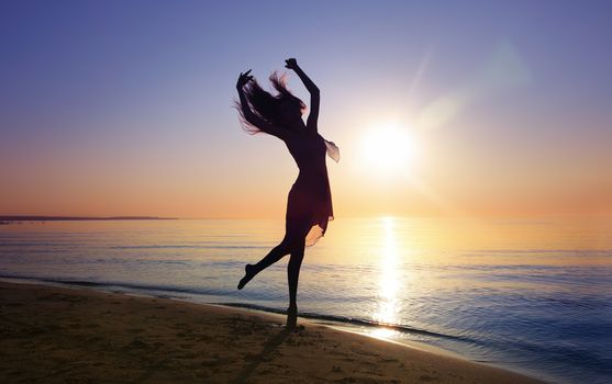 Silhouette of the woman dancing at the beach during beautiful sunset. Natural light and darkness. Artistic vivid colors added