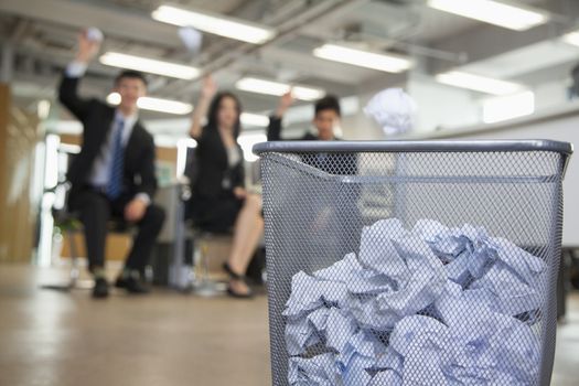 Three coworkers preparing to throw paper into waste basket 