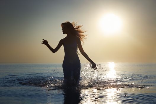 Silhouette of the woman with long hairs walking in the water during sunrise. Natural darkness and colors