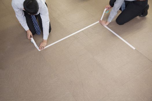 Two young businessmen taping up the floor in the office