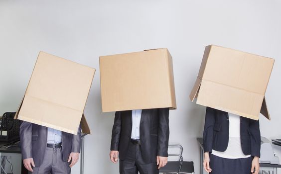 Three business people with boxes over their heads in an office