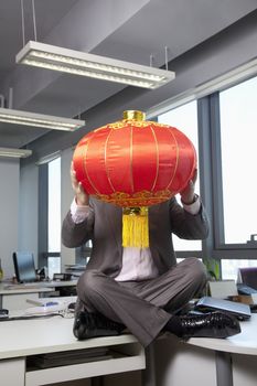 Businessman holding Chinese lantern in front of face