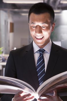 Young smiling businessman reading a book