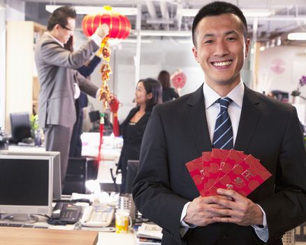 Businessman holding red envelopes and coworkers hanging decorations for Chinese new year