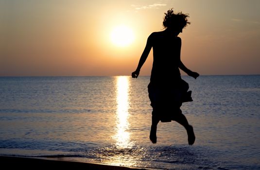 Glad lady jumps at the beach during sunset