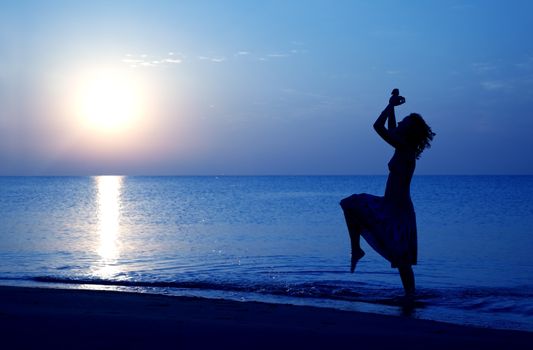 Silhouette of happy woman dancing at the beach during twilight