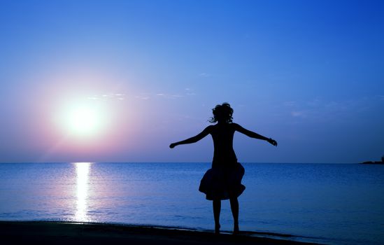 Silhouette of happy woman jumping at the beach during twilight