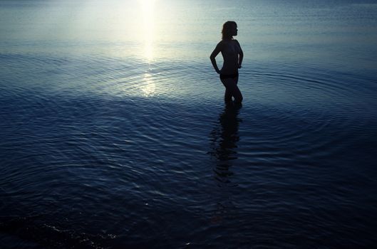 Silhouette of the topless woman standing in the water during late twilight. Natural darkness. Artistic colors added