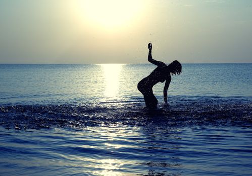 Silhouette of the happy woman playing with water at summer beach