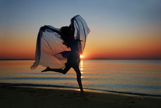 Elegant lady with fiber jumping and dancing at the morning beach during sunrise. Natural darkness and sunlight colors