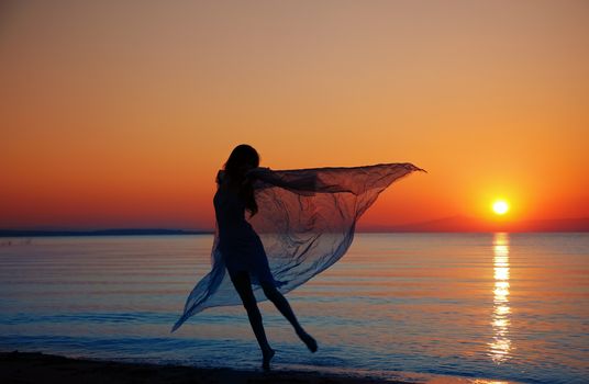 Silouette of the nifty woman dancing at the sea during sunset. Natural light and darkness. Artistic colors added