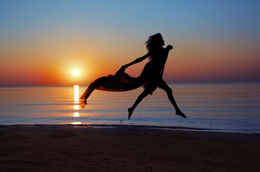 Silhouette of the woman flying at the sea during beautiful sunset. Natural light and darknesss. Vibrant colors added