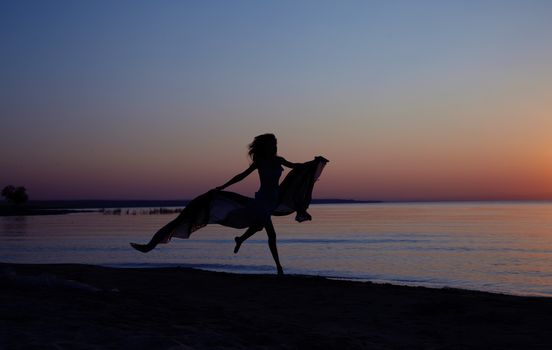 Silhouette of the woman flying at the sea during beautiful sunset. Natural light and darknesss. Vibrant colors added