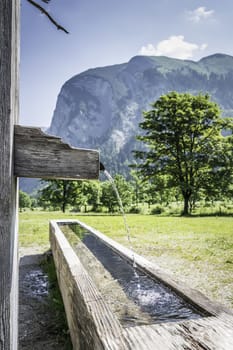 Picture of a drink fountain with running water in the Austrian Alps with mountains and trees in summer