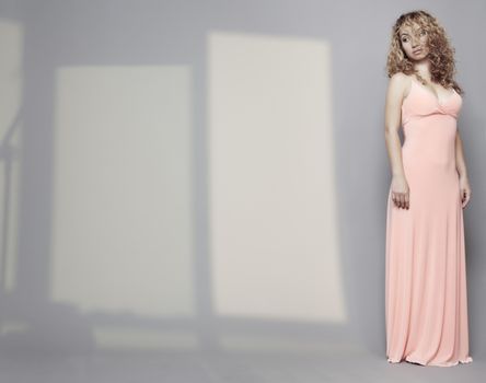 Woman in pink dress with curly hairs standing alone in the interior with shadows