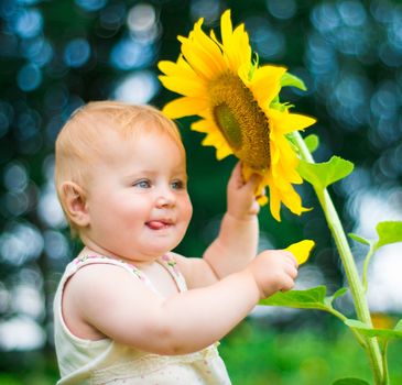Smiling baby with sunflower on summer field