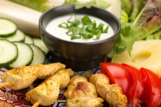 Asian food with chicken skewers, sauce, tomatoes, cucumber, pineapples, endives and salad.