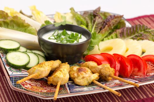 Asian food with chicken skewers, sauce, tomatoes, cucumber, pineapples, endives and salad.