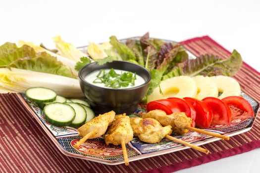 Asian food with chicken skewers, sauce, tomatoes, cucumber, pineapples, endives and salad.