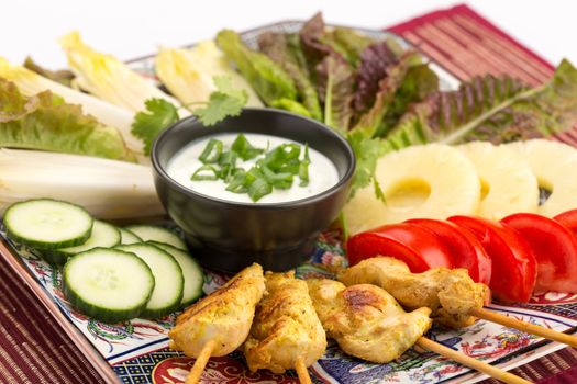 Asian food with chicken skewers, sauce, tomatoes, cucumber, pineapples, endives and salad.