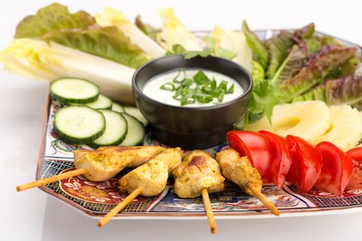 Asian food with chicken skewers, sauce, tomatoes, cucumber, pineapples, endives and salad.