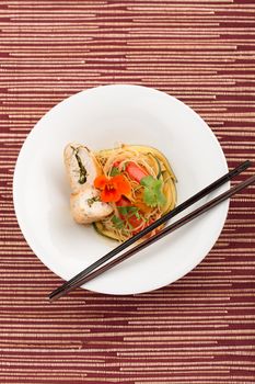 Asian food with piece of stuffed chicken, noodles, zucchini, carrots and tomatoes.