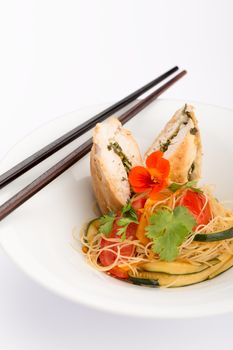 Asian food with piece of stuffed chicken, noodles, zucchini, carrots and tomatoes.