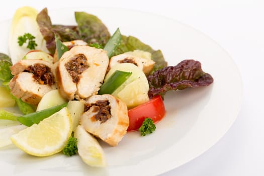 Plate of food with sliced stuffed chicken, endives, tomatoes and salad.