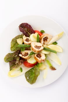 Plate of food with sliced stuffed chicken, endives, tomatoes and salad.