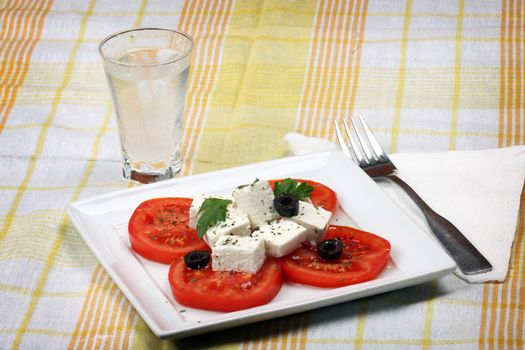 Tomato salad with feta cheese, sliced olives and glass of uzo