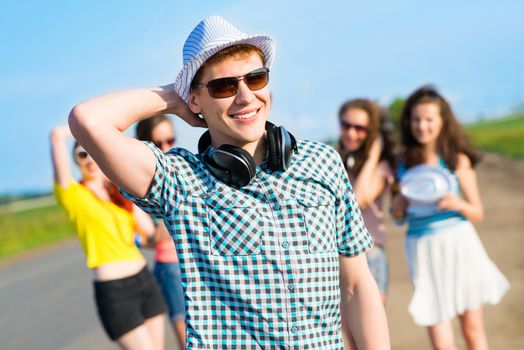 young man in sunglasses, a hat holds a hand on a background of blue sky and friends