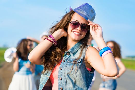 stylish young woman in sunglasses on the background of blue sky and friends