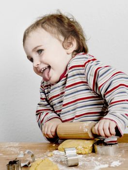 cute, laughing child with dough and rolling ping grey background. horizontal image