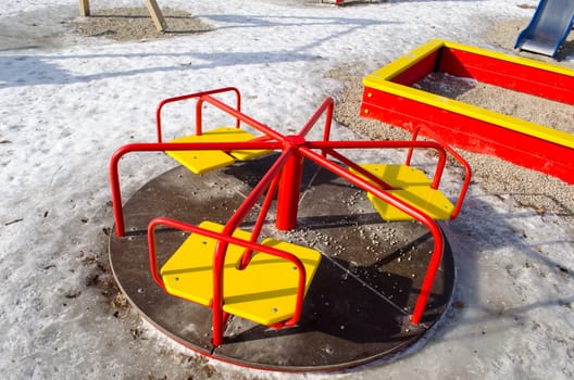 playgrounds carousel with yellow chairs and red rails in winter