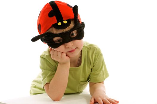 Little Boy in Green T-Shirt, Ladybug Mask and Hat Leaning on Hand White Surface isolated on white background