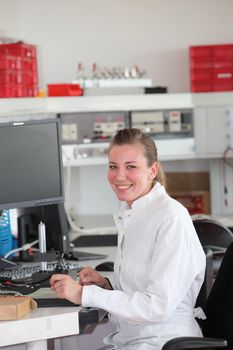 Smiling confident female technician smiling at the camera seated at her desk in a modern laboratory wearing a white lab coat