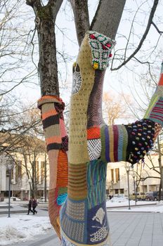 tree trunk dressed with knitted woollen wool cloth and people in winter park. modern city art.