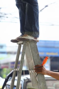 Team work of technician and his assistant, one stands on top of ladder and one hold ladder's leg