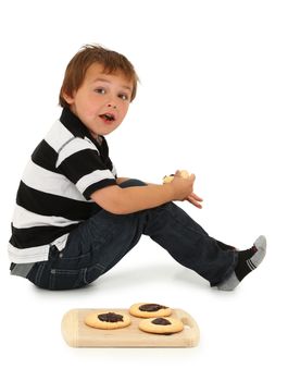 Adorable six year old Caucasian boy sitting on floor eating sugar cookies with chocolate center.