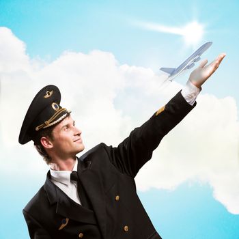 pilot in the form of extending a hand to a flying airplane on the background of clouds and sun