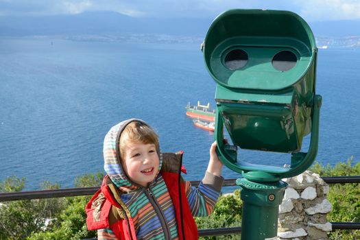 boy stands at the telescope in Gibraltar and smiling
