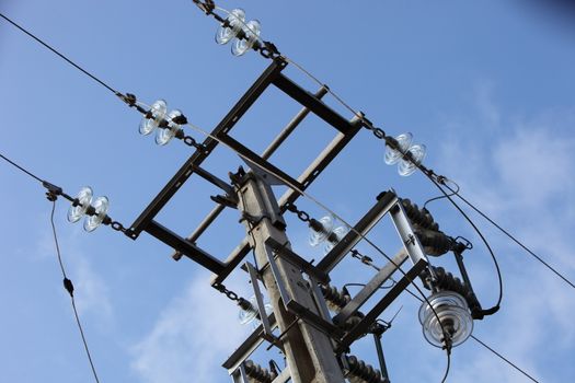 Overhead electricity pole against a blue sky with high voltage cables, insulators and conductors