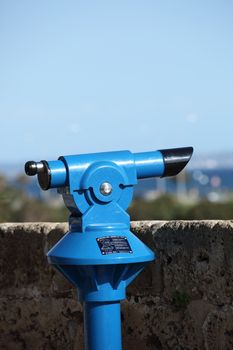 Blue metal monocular tourist viewing telescope mounted in an elevated position overlooking a town or scenic countryside