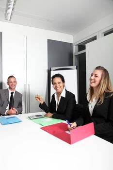 Motivated young businesswomen smiling as they sit around a table in a meeting discussing a business strategy with a male colleague