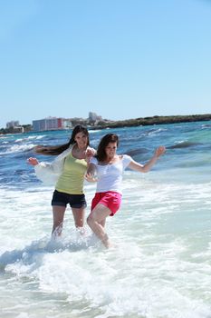 Two women frolicking in the sea splashing around in the surf in their shorts as they enjoy their summer vacation