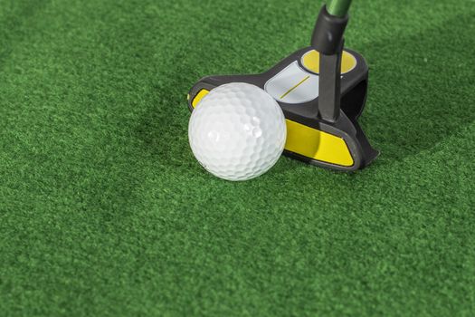 A golf ball about to be struck by a black and yellow putter.