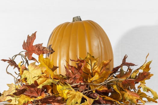 A pumpkin sitting behind a group of autumn leaves.