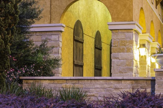 An evening view of a tuscan style front porch with rustic wooden window covers.