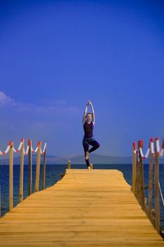 beautiful woman exercising near sea on wooden peer