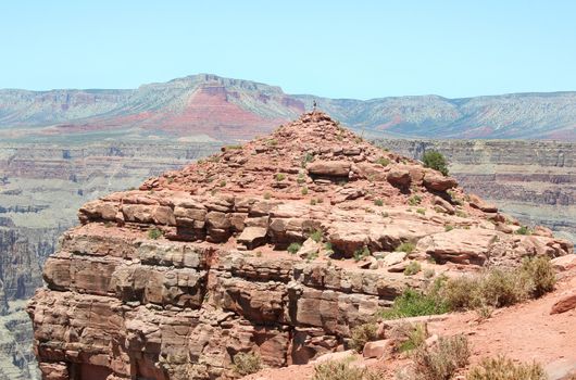 Person standing on top of the rocky knoll at Guano Point on the West Rim of the Grand Canyon. 